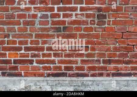 Weathered red brick wall with damages and missing joints on a grey concrete socket, use as game asset texture or reference image Stock Photo