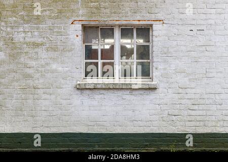 Texture shot of a window whit a white painted frame and a brick wall with thick white paint, at the bottom is a green socket of green painted bricks. Stock Photo
