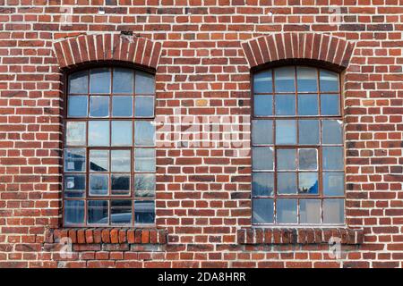 Two industrial looking windows with broken pieces of glas, the window frame is rusted, the brick wall is weathered with many imperfections. Use as gam Stock Photo