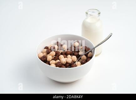 Cereal and chocolate balls in a white bowl and milk in a bottle on a light background. Stock Photo
