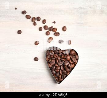 Coffee beans in the shape of a heart and grains scattered in the shape of a comet's tail on a light background. Stock Photo