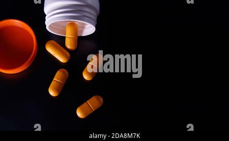 Several orange medical pills and tablets spilling out of a drug bottle. Macro top down view with copy space. Pills on black background. the view from Stock Photo