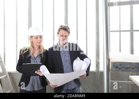 man and woman architects or engineers work together discussing with blueprint in the inside the construction building site Stock Photo