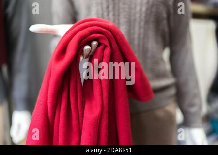 clothes in a shop, red cashmere scarf in a showroom, clothing store, woollen products, mannequin exposing elegant classic cloth, piece of red textile Stock Photo