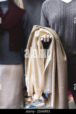 Title: A mannequin with light beige cashmere fabric in hand. Natural pashmina clothing. Woollen shop. close up of a person holding a scarf Stock Photo