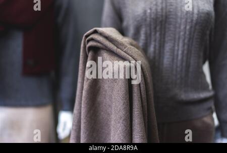 A mannequin with dirty brown cashmere fabric in hand. Dark grey clothing. Woollen shop. close up of a person holding a scarf Stock Photo