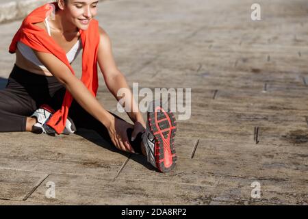 Cropped shot of attractive fitness woman stretching leg and smiling, doing warm-up exercises before running Stock Photo