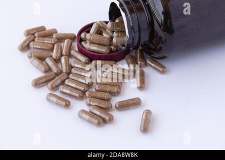 Amber plastic bottle with brown lid dropped open, with many pills of a drug or dietary supplement spilling out of the bottle on a white surface Stock Photo
