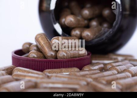 Amber plastic bottle with brown lid dropped open, with many pills of a drug or dietary supplement spilling out of the bottle on a white surface Stock Photo