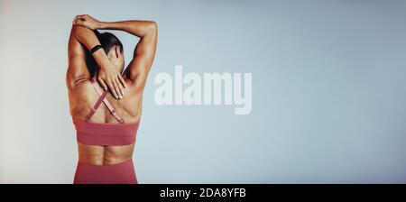 Rear view of fitness woman doing arm stretching exercises. Female athlete doing warm up before workout. Stock Photo