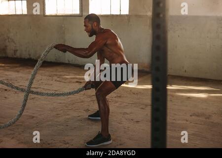 fitness man workout with battle ropes inside abandoned warehouse. Muscular man doing battle rope workout. Stock Photo
