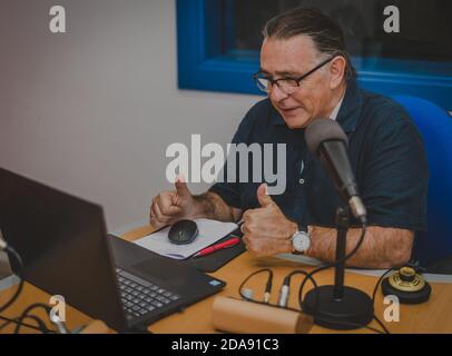 Adult man makes video conference with laptop in his radio studio and makes well gesture Stock Photo