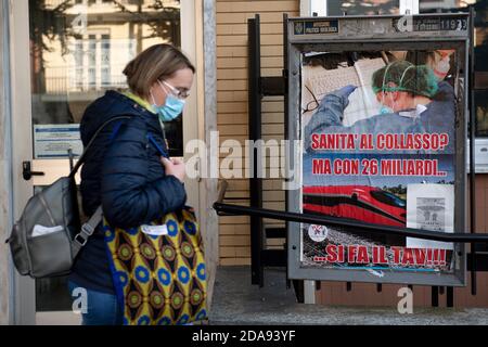 Turin, Italy. 10th Nov, 2020. TURIN, ITALY - November 10, 2020: A woman walks past a sign reading 'Health to collapse? But with 26 billion you make the TAV (high-speed railway)!' In many Italian region hospitals struggle to find space for coronavirus patients during the second wave of COVID-19 pandemic. (Photo by Nicolò Campo/Sipa USA) Credit: Sipa USA/Alamy Live News Stock Photo