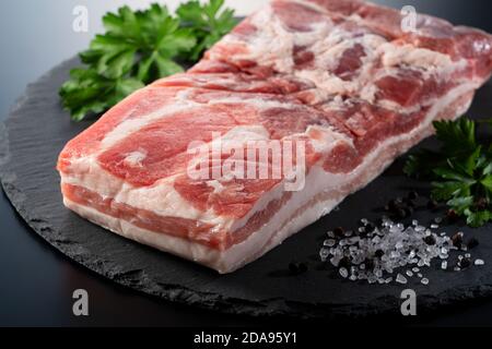 Pork belly, black pepper, rock salt and Italian parsley on a black stone tray. Stock Photo