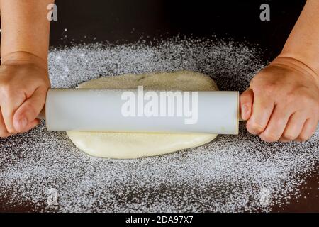 Rolling pin in woman hand and white sugar paste on table. Stock Photo