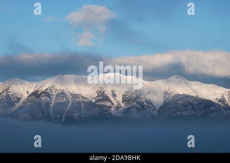 The sun rises on the snow-capped east slope of the Lemhi Range shrouded in clouds on a winter morning.