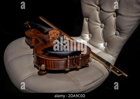 Still life musical instrument. Violin and bow on a white leather chair Stock Photo