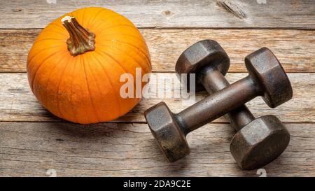 a pair of vintage iron rusty dumbbells on a rustic barn wood background with a pumpkin, fitness during fall holidays concept Stock Photo