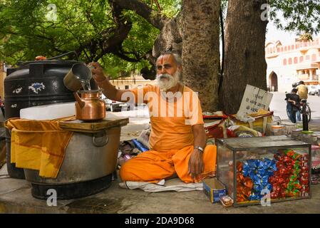 Old Rajasthani man wearing traditional dress pouring drinking water in copper vessel thirsty people city palace hot summer day Jaipur Rajasthan India. Stock Photo