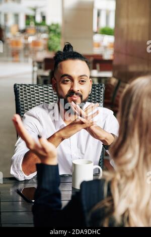 Smiling excited young entrepreneur listening to talking colleague at meeting in cafe Stock Photo