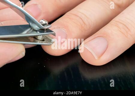 hand manicure with nail clipper. close up over black background. self-cutting nails. close-up nail cutting Stock Photo