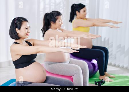 Group of happy young Asian pregnant women sitting on fitness balls and doing exercise for arms Stock Photo