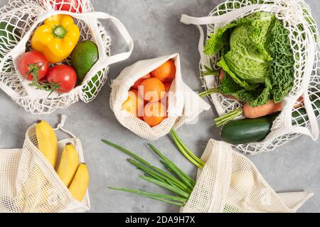 Fresh vegetables and fruits in tote eco friendly bags on grey table top view. Eco shopping concept. Healthy raw eating. Stock Photo