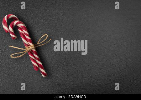 Christmas card with candy canes. Candy Canes On Black Stone. Christmas candy canes tied in a bundle. Space for your text. flatlay. top view Stock Photo