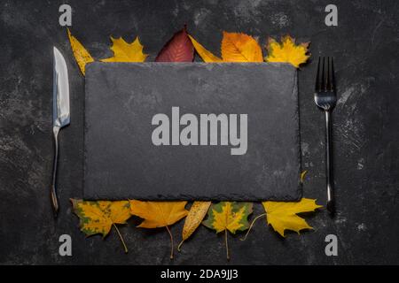 Autumn layout with still life of black stone tray, autumn leaves, fork and knife. Autumn, top view. Stock Photo