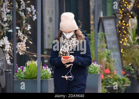 Girl with glasses and mask checking the smartphone in the street during Covid or Coronavirus emergency, Christmas and New Year 2021 background Stock Photo