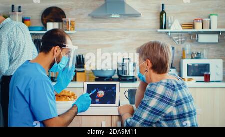 Caregiver social worker discussing about coronavirus with senior patient during home visit. Male nurse at elderly retired woman visit explaining covid-19 spreading, help for people in risk group Stock Photo