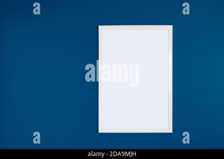 White blank frame hanging on the interior blue wall. Empty frame mock up. Stock Photo