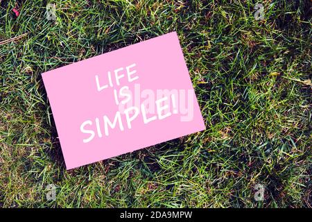 Life is simple motivational quote written on paper on green grass background. Peaceful, easy, comfortable and simplified life concept. Stock Photo