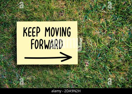 The words keep moving forward written on paper on green grass background. Inspirational quote for persistence, progress or improvement in business or Stock Photo