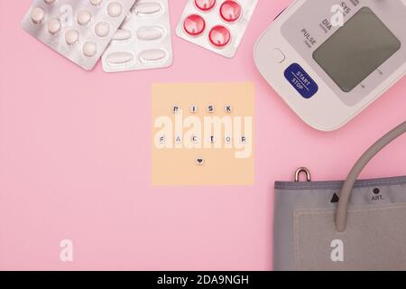 Concept of health, cardiology, heart disease. The words 'RISK FACTOR' on the blocks. Blood pressure monitor, tablets on a pink background. Top view, f Stock Photo