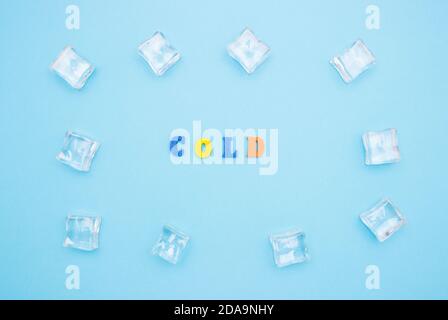 The word COLD on a blue background of wooden multicolored letters, ice cubes around the word. Stock Photo