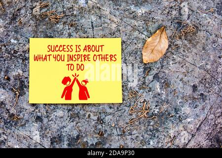 Success is about what you inspire others to do inspirational motivational quote written on yellow paper a rock background in nature. Stock Photo