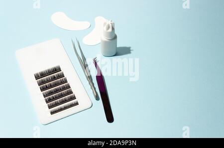 Artificial eyelashes on a white tablet, glue, patches and tweezers with shadow on a blue background. Free space for text, side view. Tools for lashmak Stock Photo