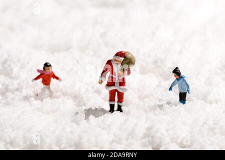 Miniature Father Christmas or Santa Claus carrying a sack of gifts walking through thick white winter snow accompanied by a young girl and boy with co Stock Photo