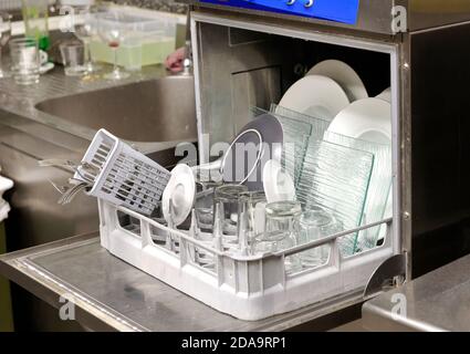 Open dishwasher filled with clean dinnerware and glassware in a small restaurant kitchen in close up on the machine Stock Photo