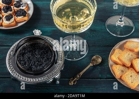 Caviar in a vintage bowl with a champagne coupe glass, with bread and toasts, on a dark blue wooden background