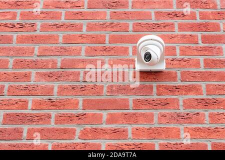 Low angle view on white cctv security camera mounted on a red brick wall. Security concept, big brother is watching Stock Photo