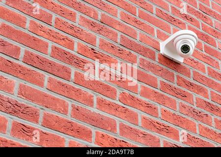Low angle view on white cctv security camera mounted on a red brick wall. Security concept, big brother is watching Stock Photo