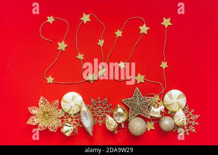 Collection of golden Christmas objects viewed from above on red background. 2021 lettering from beads. Stock Photo