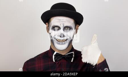 A horrible man in clown makeup smiles and shows a thumb up. A scary clown looks at the camera and laughs terribly. Stock Photo