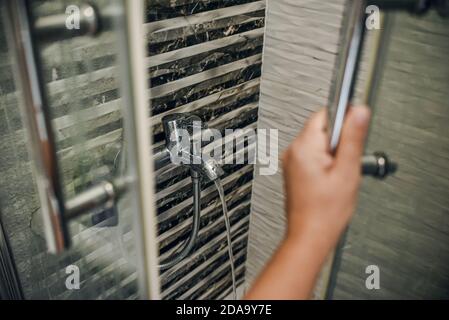 hand opens the door to the gray shower stall. a stream of water flows from the water tap Stock Photo