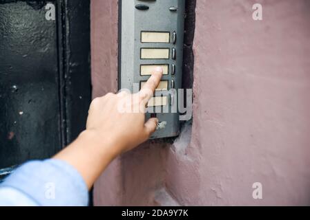 hand in a denim jacket reaches for the doorbell. finger presses the doorbell. the street door. Stock Photo