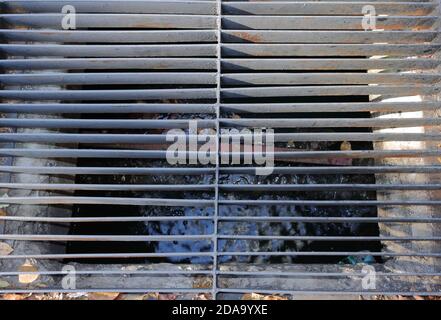 Closeup steel gutter cover on roadside with blurred motion of waste water inside, high angle view Stock Photo