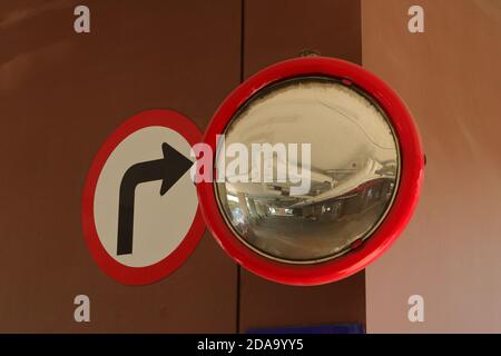 An old cracked convex mirror mounted on brown wall at the corner of parking lot of a building, safety concept