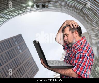 Problems with computer. Middle aged stressed businessman working on laptop against urban background Stock Photo